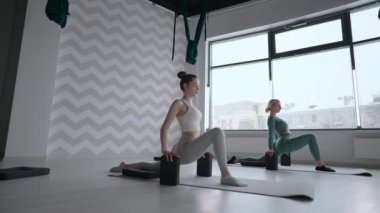 Pencereli spor salonunda esneme hareketleri yapan bir grup genç kadın. İki çekici spor kızı fitness dersinde nauka asana tekne yoga pozu veriyor. Yoga stüdyosunda bacak bacak esneten iki kadın.
