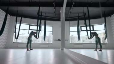Genç, gülümseyen kadın salıncakta sallanıyor. Havadan uçan yoga egzersizleri fitness kulübündeki yeşil hamakta pratik yapıyor.