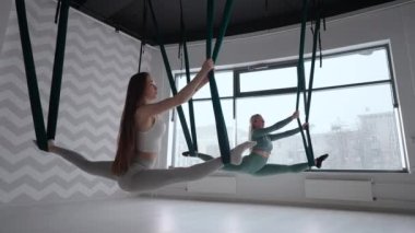 Antrenör ve genç bir kadın spor salonunda jimnastik yapıyor. İki güzel Yogi kadını, spor salonunda yeşil hamaklarda hava yogası yapıyorlar.