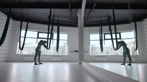 Młoda uśmiechnięta kobieta ćwiczy w aero rozciągając huśtawkę. Latające ćwiczenia jogi lotniczej w zielonym hamaku w klubie fitness — Wideo stockowe