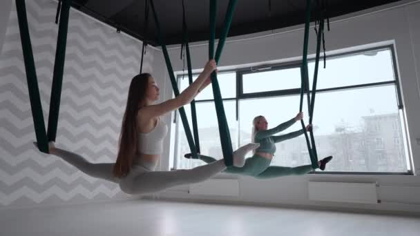 Antrenör ve genç bir kadın spor salonunda jimnastik yapıyor. İki güzel Yogi kadını, spor salonunda yeşil hamaklarda hava yogası yapıyorlar. — Stok video