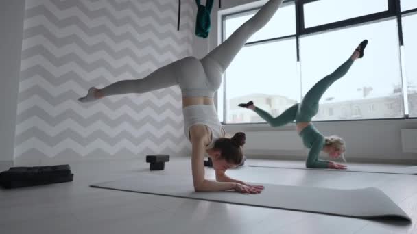 Gruppo di giovani donne che si allungano in palestra con le finestre. Due attraenti ragazze sportive lavorano fuori Nauka asana barca yoga posa sul tappeto nero in classe di fitness. Due donne che allungano le gambe insieme nello studio di yoga — Video Stock