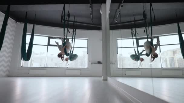 两名女子的室内射击练习了不同的逆反重力瑜伽，在瑜伽工作室里有一个吊床。精神与身体的平衡，两个人的努力与成就的概念 — 图库视频影像