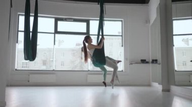 İki genç yogi kadın spor salonunda yeşil hamaklarda hava yogası yapıyorlar. Güzel kadınlar sınıfta çalışıyor, aero yogası yapıyorlar. Parsvottanasana, Piramit pozu