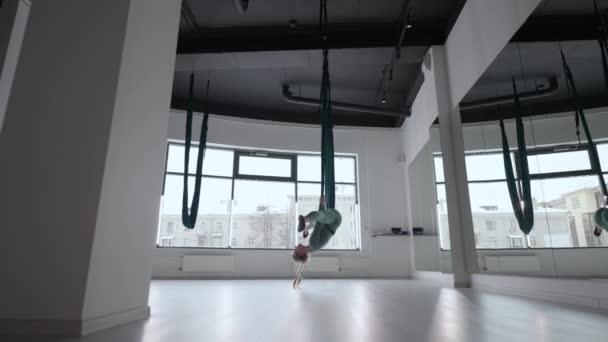 Привлекательный тренер по фитнесу делает антигравитационные аэродинамические упражнения йоги в зеленом гамаке. Молодая гибкая женщина практикуется в аэрорастяжении качели в фитнес-клубе. Концепция женской фитнес-йоги — стоковое видео