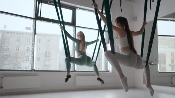 Trainer en jonge vrouw oefenen aero gymnastiek met schorsingen in de sportschool. Groep van twee jonge mooie yogi vrouwen doen luchtyoga praktijk in groene hangmatten in fitness club — Stockvideo