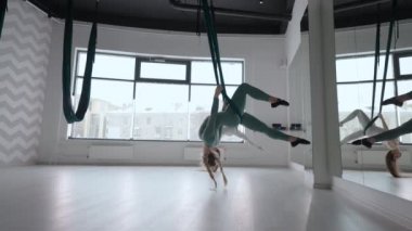 İki genç yogi kadın spor salonunda yeşil hamaklarda hava yogası yapıyorlar. Güzel kadınlar sınıfta çalışıyor, aero yogası yapıyorlar. Parsvottanasana, Piramit pozu