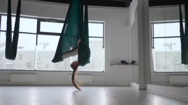 Young beautiful woman practice in aero stretching swing. Young woman rolls her head upside down in a hammock for aerial yoga. Focused pretty mature woman doing aerial yoga in gym — Stock Video