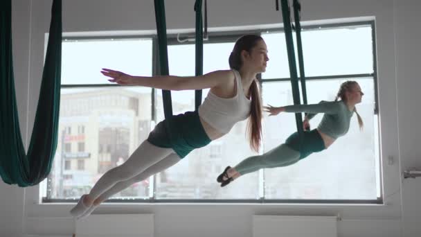 Тренер і молода жінка практикують аерогімнастику з суспензіями в спортзалі. Група з двох молодих красивих йогів, які практикують повітряну йогу в зелених гамаках у фітнес-клубі — стокове відео