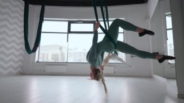 İki genç yogi kadın spor salonunda yeşil hamaklarda hava yogası yapıyorlar. Güzel kadınlar sınıfta çalışıyor, aero yogası yapıyorlar. Parsvottanasana, Piramit pozu