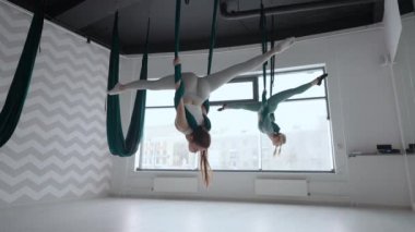 Antrenör ve genç bir kadın spor salonunda jimnastik yapıyor. İki güzel Yogi kadını, spor salonunda yeşil hamaklarda hava yogası yapıyorlar.