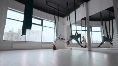 Antrenör ve genç bir kadın spor salonunda jimnastik yapıyor. İki güzel Yogi kadını, spor salonunda yeşil hamaklarda hava yogası yapıyorlar.