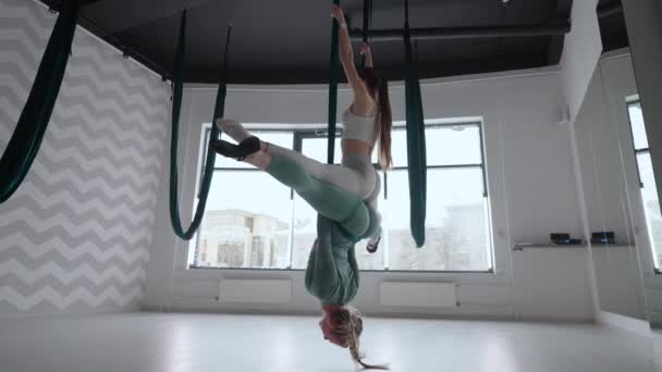 Entrenadora y joven practicante de gimnasia aérea con suspensiones en el gimnasio. Grupo de dos jóvenes hermosas mujeres yoguis haciendo práctica de yoga aéreo en hamacas verdes en el gimnasio — Vídeo de stock