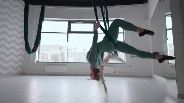 Twee jonge yogi vrouwen die luchtyoga beoefenen in groene hangmatten in een fitnessclub. Mooie vrouwen die trainen in de klas, aero yoga doen. Variatie van Parsvottanasana, piramide pose — Stockvideo