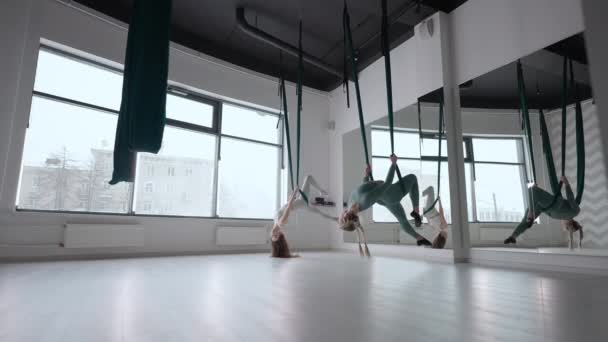 Entraîneur et jeune femme pratiquant l'aérogymnastique avec suspensions au gymnase. Groupe de deux jeunes belles femmes yogi faisant de la pratique du yoga aérien dans des hamacs verts dans un club de fitness — Video