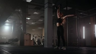 Güçlü bir kadın çaba sarf eder ve zorlukların üstesinden gelir. Karanlık bir spor salonunda bir dambılı kaldırır. Spor salonunda spor salonundaki ağırlık kaldıran kadın..