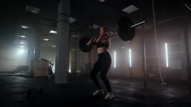 Bodybuilderin beim Training mit Gewichten im Fitnessstudio. Eine Gewichtheberin führt in einer dunklen Turnhalle ein Hantelheben durch. Bodybuilderin macht Gewichtheben-Übungen im Hardcore-Training — Stockvideo