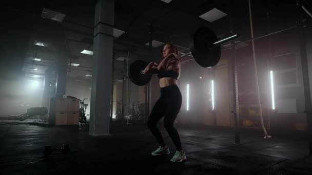 Mujer culturista haciendo ejercicio con pesas en el gimnasio. una mujer levantadora de pesas realiza un levantamiento de pesas en un gimnasio oscuro. Mujer culturista hace ejercicios de levantamiento de pesas en el entrenamiento duro — Vídeo de stock