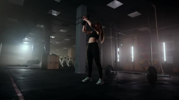 Una mujer fuerte hace esfuerzos y superar las dificultades levanta una mancuerna en un gimnasio oscuro. Fitness mujer levantamiento de pesas pesas pesas entrenamiento en gimnasio club. — Vídeo de stock