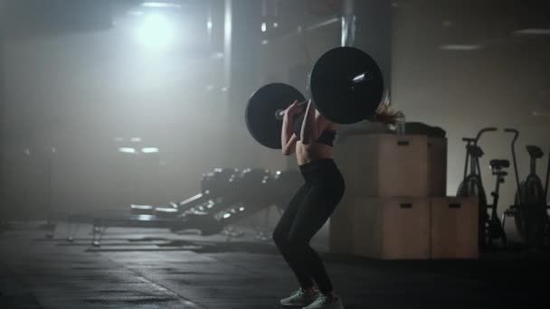 Bodybuilderin beim Training mit Gewichten im Fitnessstudio. Eine Gewichtheberin führt in einer dunklen Turnhalle ein Hantelheben durch. Bodybuilderin macht Gewichtheben-Übungen im Hardcore-Training — Stockvideo