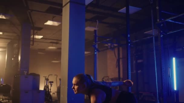 Una mujer fuerte hace esfuerzos y superar las dificultades levanta una mancuerna en un gimnasio oscuro. Fitness mujer levantamiento de pesas pesas pesas entrenamiento en gimnasio club. — Vídeo de stock