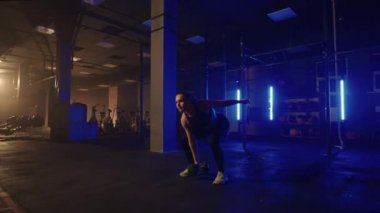 Güçlü bir kadın çaba sarf eder ve zorlukların üstesinden gelir. Karanlık bir spor salonunda bir dambılı kaldırır. Spor salonunda spor salonundaki ağırlık kaldıran kadın..