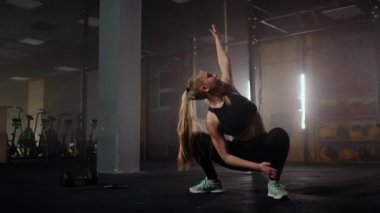 Genç, narin bir kadın antrenmandan önce hazırlanıyor ve ısınıyor. Spor salonunun karanlık iç kısımlarında yapılan yorucu bir çalışmadan sonra kasları germek ve otostop çekmek.