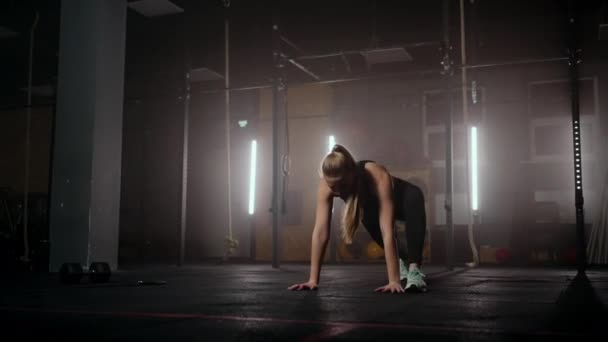 Egy nő gyakorolja a nyújtást egy sötét fitneszteremben edzés után, a Fitness nő a sötét edzőteremben a magizmokon dolgozik. — Stock videók