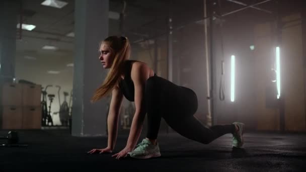 Une femme fait des exercices d'étirement dans une salle de fitness sombre après une séance d'entraînement, femme de fitness travaillant sur les muscles de base à la salle de gym sombre — Video