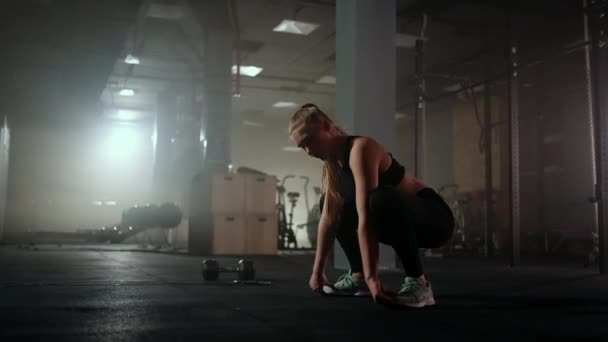 Una joven esbelta se prepara y se calienta antes de entrenar. Enganche y estiramiento de los músculos después de un tedioso entrenamiento duro en el interior oscuro de la sala de fitness — Vídeos de Stock