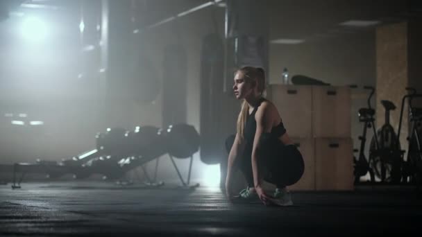 Młoda szczupła kobieta przygotowuje się i rozgrzewa przed treningiem. Bicie i rozciąganie mięśni po uciążliwym ciężkim treningu w ciemnym wnętrzu sali fitness — Wideo stockowe