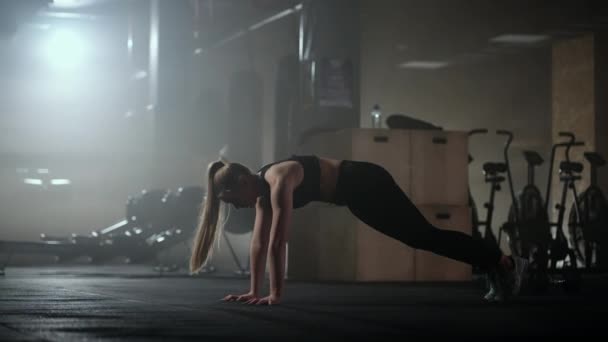 Een vrouw doet stretching oefeningen in een donkere fitnessruimte na een training, Fitness vrouw uit te werken op de kern spieren in donkere fitnessruimte — Stockvideo