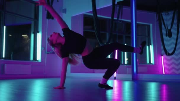 Een vrouw danst in een studio met een neon licht die sierlijke oefeningen en bewegingen uitvoert van stretchen en dansen in slow motion — Stockvideo