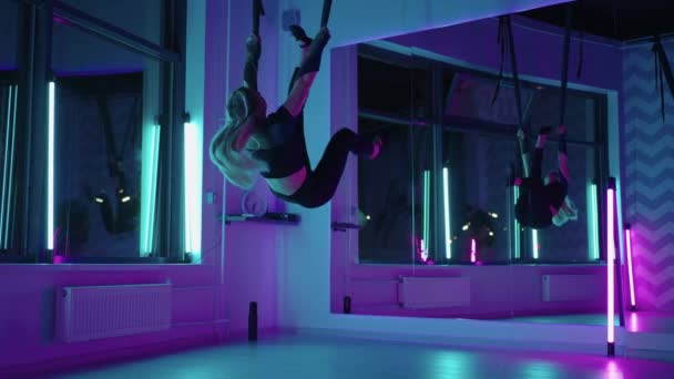 Kobieta uprawia jogę i rozciąga się na wiszącym hamaku w neonowym świetle. młody dość szczupły ciało fitness dziewczyna praktykuje mucha joga w siłowni. — Wideo stockowe