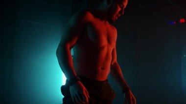 Yorgun bir sporcu ağır çekimde egzersiz yaptıktan sonra neon ışıklı bir halterde otururken ağır ağır nefes alıyor. İyileş ve yeni bir atılım için hazırlan.