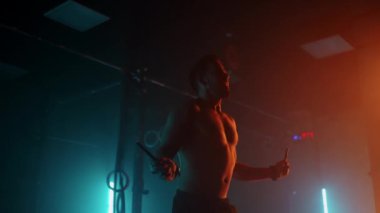 Çıplak gövdeli kaslı adam atlamak için ip kullanıyor. İp atlayan erkek boksör. Yavaş çekimde dumanla renkli ışıkta ip atlama egzersizleri yapan dövüşçü..