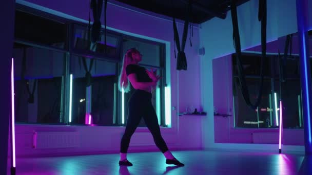 Een vrouw danst in een studio met een neon licht die sierlijke oefeningen en bewegingen uitvoert van stretchen en dansen in slow motion — Stockvideo