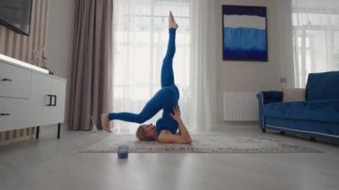 Evde bir kadın evden çıkmadan yoga egzersizleri yapıyor. Evde eğitim. Mavi takım elbiseli bir kadın halıda antrenman yapıyor.