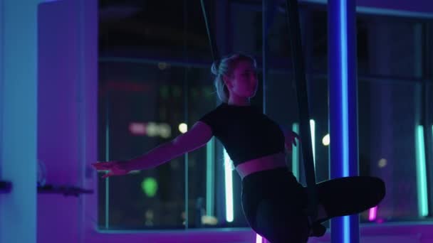 Kobieta uprawia jogę i rozciąga się na wiszącym hamaku w neonowym świetle. Kobieta lata w hamaku w studio, ćwicząc rozciąganie i ciało. Ćwiczenia w powietrzu — Wideo stockowe