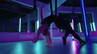 Baş aşağı asılı duran ve yoga hamağı salıncağı kullanan bir kadın yerçekimi yogası yapıyor. Yerçekimi yogası pozu vermek için hamak kullanan güzel genç bir kadının arka görüntüsü.