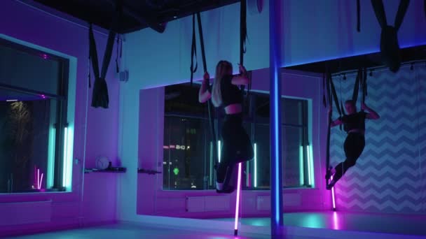 Uma mulher faz ioga esportivo no ar em uma rede em luz de néon realizando exercícios e movimentos graciosos de alongamento e dança em câmera lenta. — Vídeo de Stock