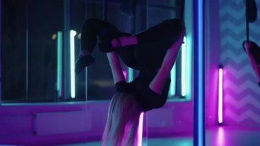 Bir kadın yoga yapıyor ve neon ışıkta asılı bir hamakta geriniyor. Bir kadın stüdyoda hamakta uçuyor, esneme hareketleri yapıyor ve vücut egzersizleri yapıyor. Havadaki egzersizler.