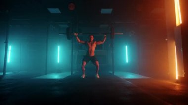 Mavi-turuncu neon ışıklı erkek kaldırıcı spor salonunda antrenmana hazırlanıyor. Çıplak gövdeli güçlü bir adam halteri başının üzerine kaldırır. Ağırlık kaldırma egzersizi yapar..