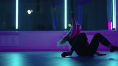 Bir kadın yoga yapıyor ve neon ışıkta asılı bir hamakta geriniyor. Bir kadın stüdyoda hamakta uçuyor, esneme hareketleri yapıyor ve vücut egzersizleri yapıyor. Havadaki egzersizler.