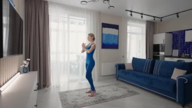 Öğleden sonra evde yoga yaparken halıda, kanepenin yanında ve oturma odasındaki TV 'de. Sabah egzersizleri ve yoga dersleri. Denge ve dayanıklılık için karmaşık yoga egzersizleri