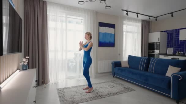 Allenamento di yoga a casa sul tappeto nel pomeriggio vicino al divano e alla TV nel soggiorno. Esercizi mattutini e lezione di yoga. Esercizi complessi di yoga per equilibrio e resistenza — Video Stock