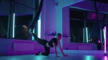 Bir kadın yoga yapıyor ve neon ışıkta asılı bir hamakta geriniyor. Genç, zayıf vücut formundaki kız spor salonunda sinek yogası yapıyor..