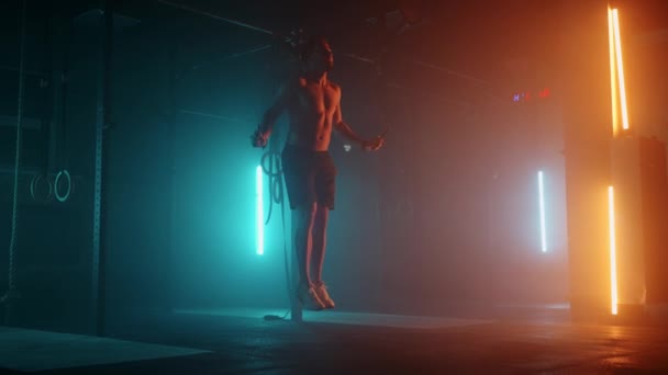 Svalnatý muž s holým trupem skáká přes švihadlo. Mužský boxer se skákacím lanem. Bojovník dělá skok lano cvičení v barevném světle s kouřem ve zpomaleném filmu. — Stock video