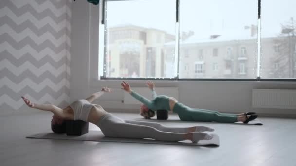 若い女性2人がキューブドプラットフォーム上に横たわるバック演習を実行します。背中の筋肉の伸展とトーン。姿勢の改善 — ストック動画