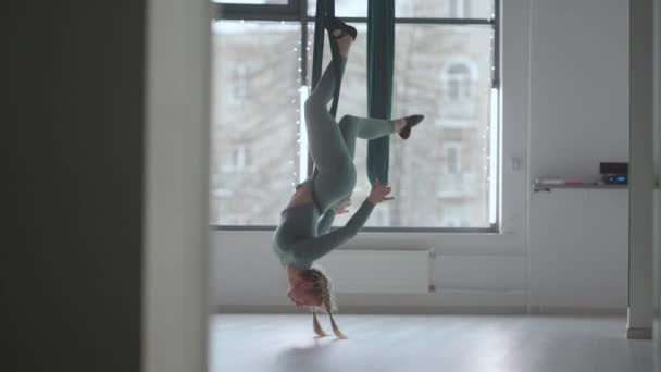 Una joven hermosa mujer realiza ejercicios en una hamaca de aero yoga. Una mujer en la tarde delante del espejo en el pasillo realiza estiramiento solo — Vídeos de Stock